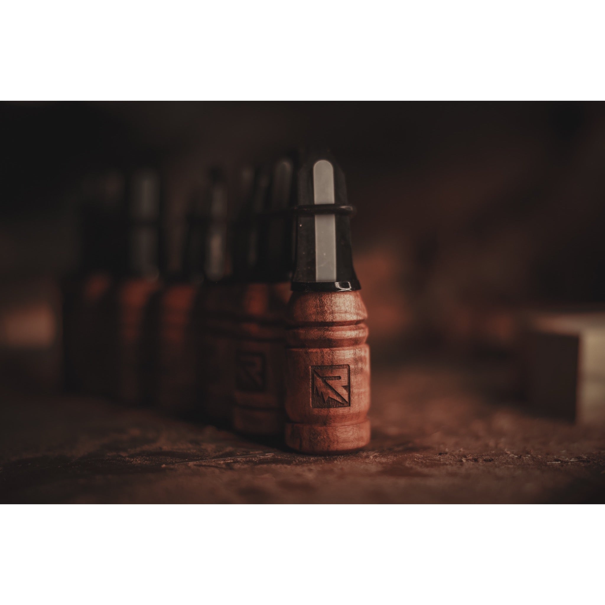 A row of Riven Menace-Maple wooden and black plastic objects with engraved arrow symbols rests on a textured surface, set against a blurred background and warm lighting.