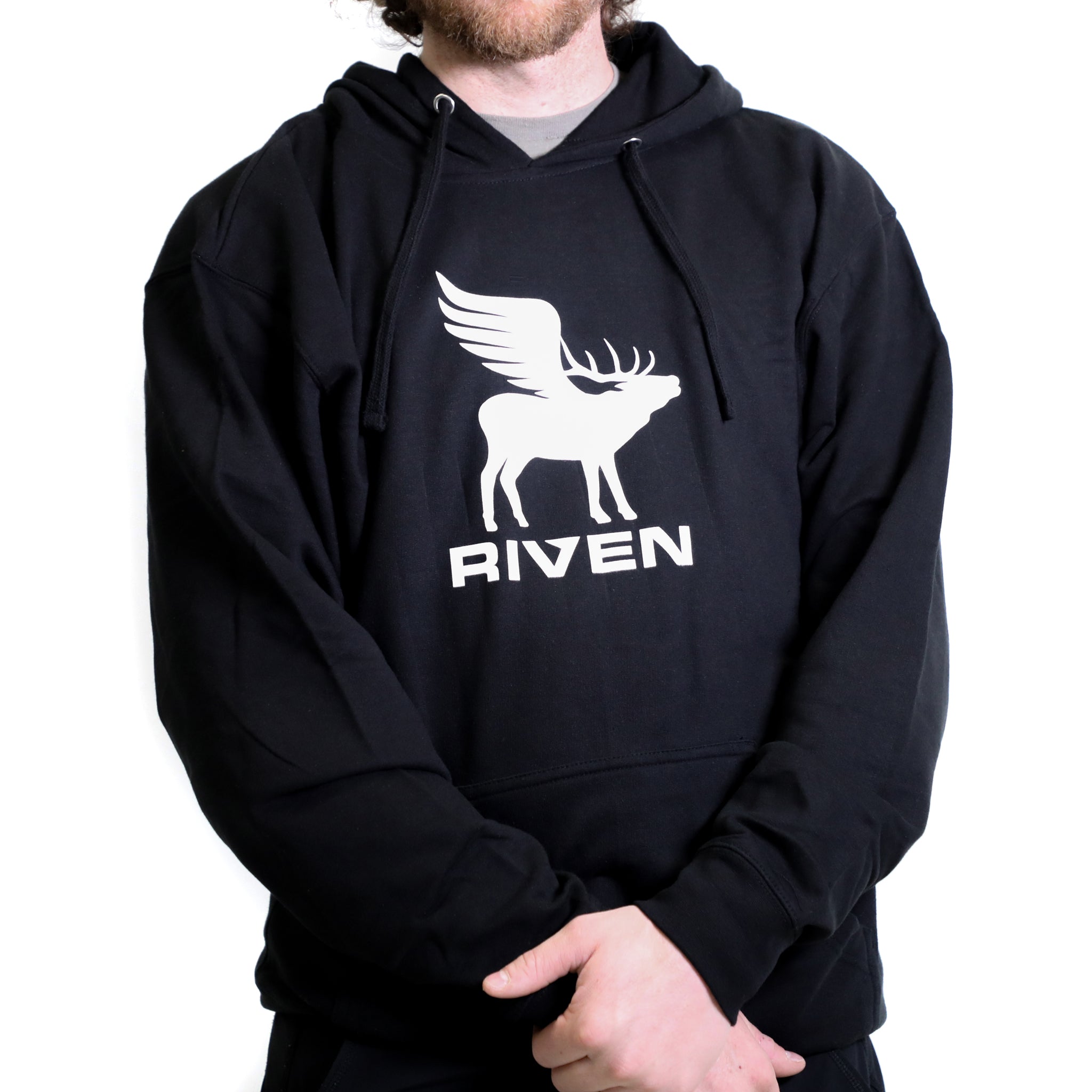 A person wearing the Riven Flying Elk Hoodie, featuring a white graphic of a winged deer and the brand name on the front, stands against a white background.