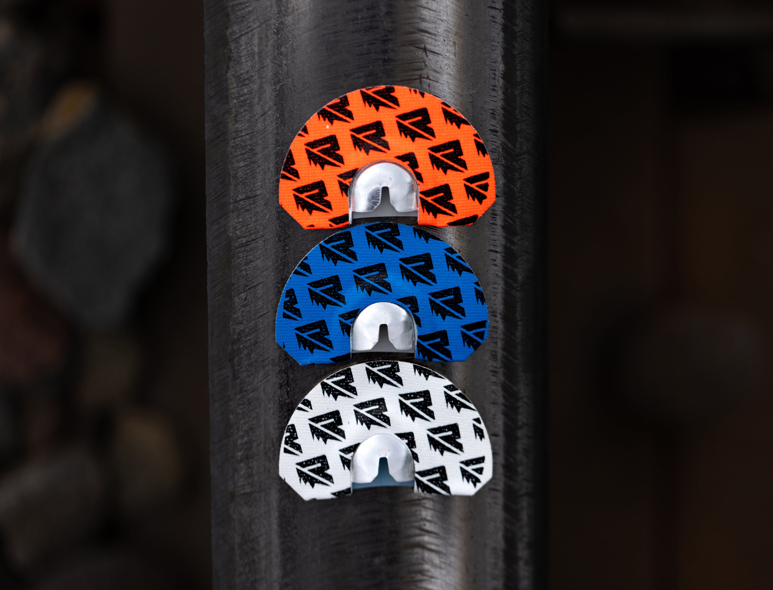 The Riven Rebel Series Bundle features three semi-circular plastic tools in orange, blue, and white with repeating black arrow logos, stacked vertically on a textured dark metallic surface.